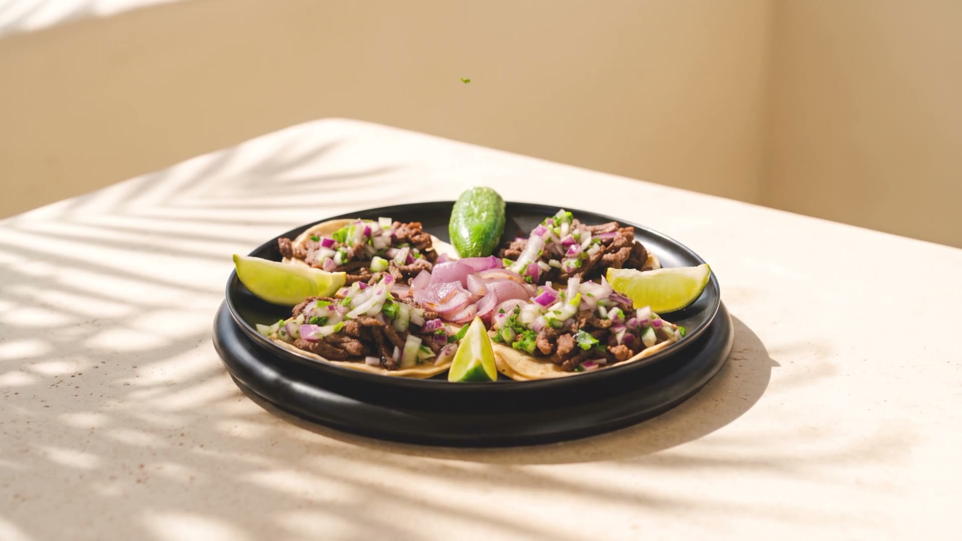 Four carne asada street tacos with lime, grilled onion and a roasted jalapeño on a dark stone table
